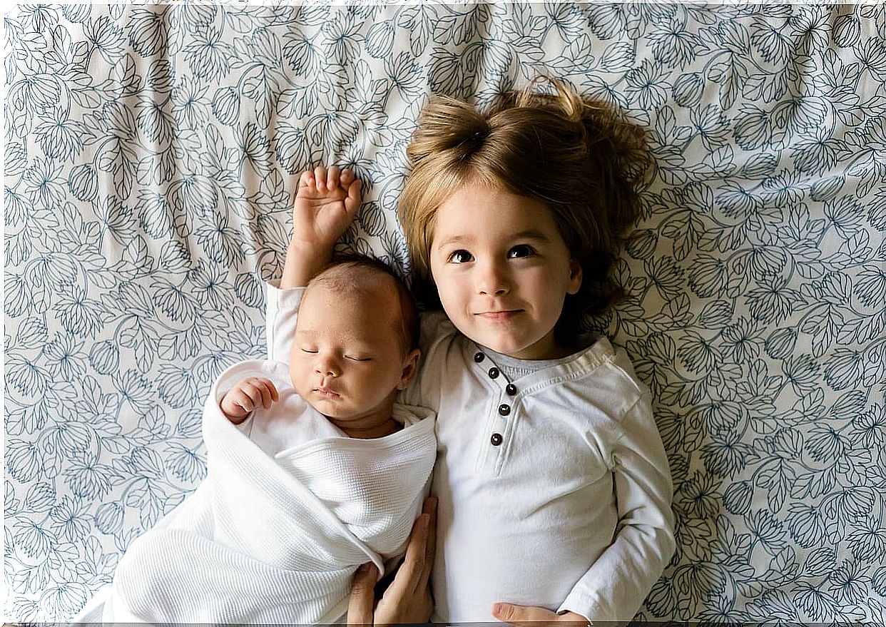 Child and newborn lying on the bed.