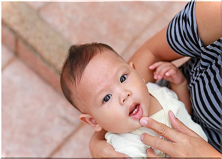 Baby showing two milk teeth with the help of his mother's hand.