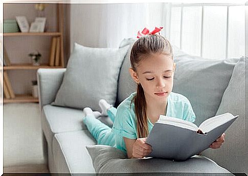 Girl lying on the couch reads a book.