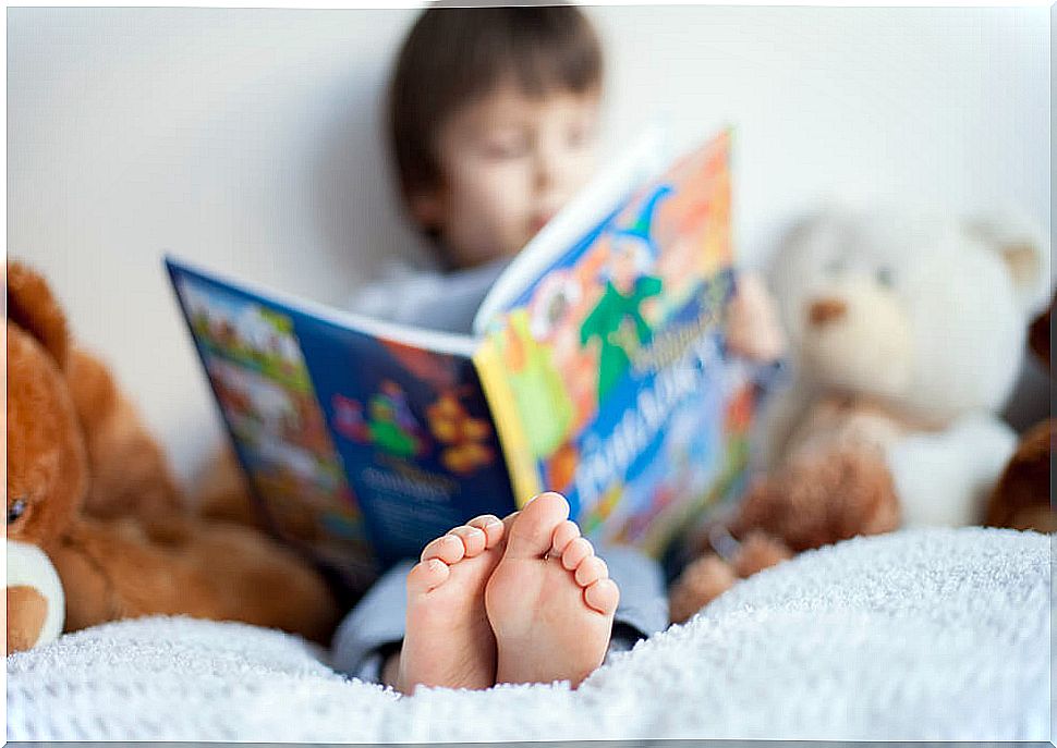 Boy sitting on the bed surrounded by soft toys reads a children's story.